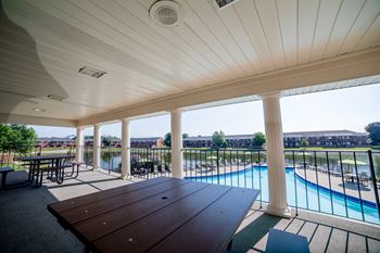 a covered patio with a picnic table and a pool in the background